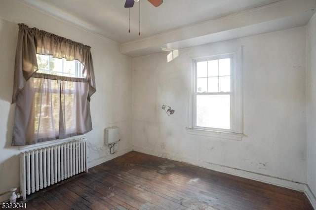 spare room with radiator heating unit, ceiling fan, plenty of natural light, and dark wood-type flooring