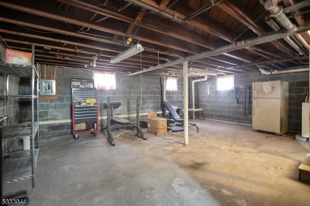 basement featuring electric panel and white refrigerator