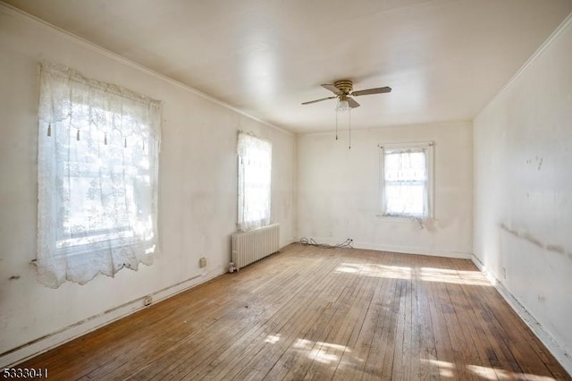 empty room with wood-type flooring, radiator heating unit, ceiling fan, and a wealth of natural light