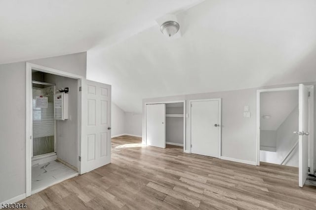 unfurnished bedroom with connected bathroom, light wood-type flooring, and vaulted ceiling