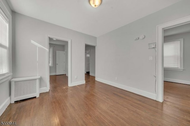 unfurnished room featuring wood-type flooring, radiator, and a wealth of natural light