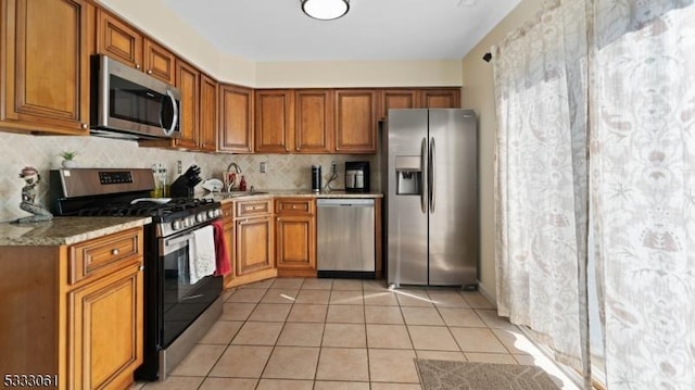 kitchen with appliances with stainless steel finishes, light stone countertops, decorative backsplash, sink, and light tile patterned flooring