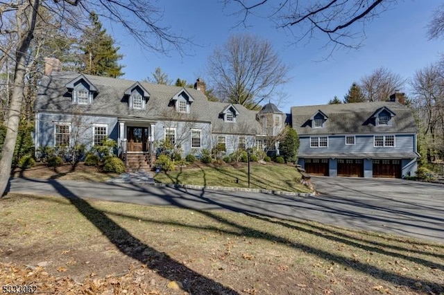 new england style home with driveway, a chimney, a garage, and a front yard