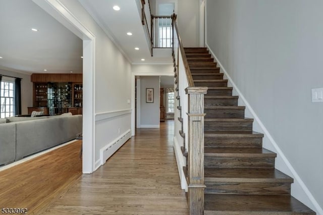 stairs with ornamental molding, a baseboard heating unit, wood finished floors, recessed lighting, and baseboards