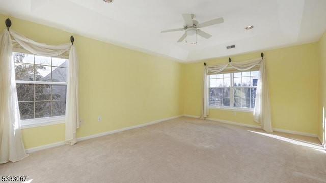 empty room featuring a raised ceiling, light carpet, and ceiling fan