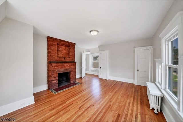 unfurnished living room featuring a brick fireplace, radiator, and light wood-type flooring