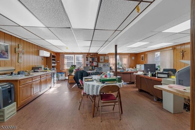 dining room with an AC wall unit, a drop ceiling, and wooden walls