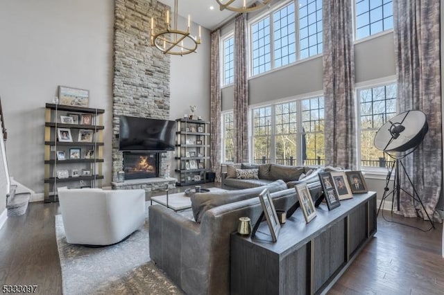 living room featuring a notable chandelier, a towering ceiling, dark wood-type flooring, and a fireplace