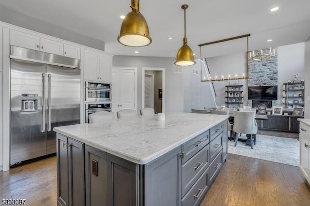 kitchen with a center island, white cabinetry, stainless steel appliances, hanging light fixtures, and dark hardwood / wood-style floors