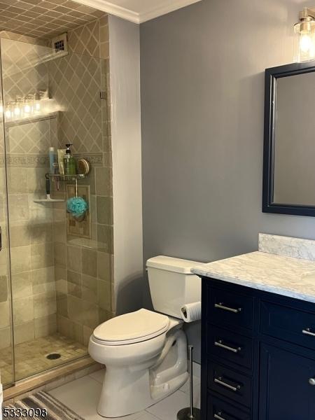 bathroom featuring tile patterned floors, a shower with door, vanity, toilet, and ornamental molding