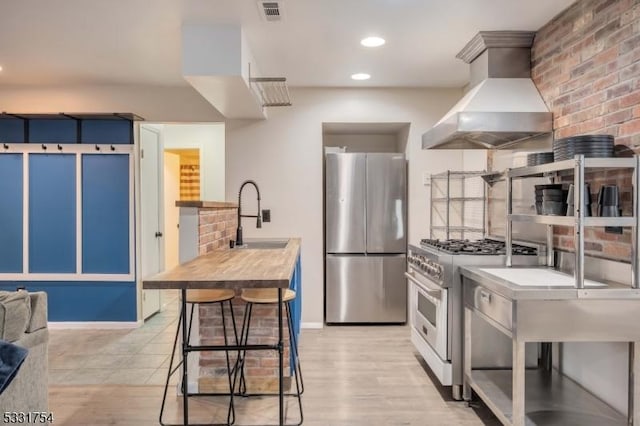 kitchen featuring appliances with stainless steel finishes, wall chimney exhaust hood, sink, light wood-type flooring, and a breakfast bar