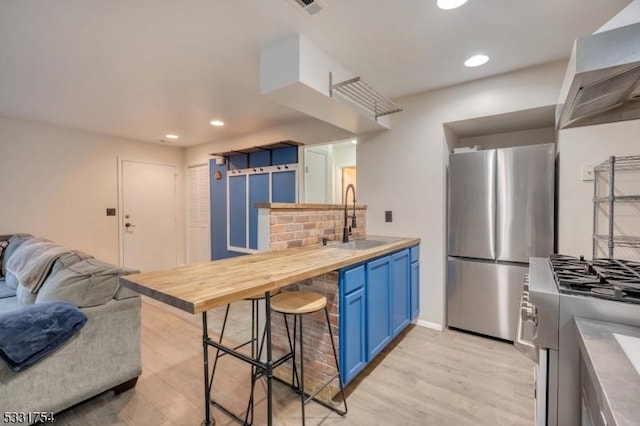 kitchen with stainless steel appliances, sink, blue cabinetry, butcher block countertops, and light hardwood / wood-style flooring