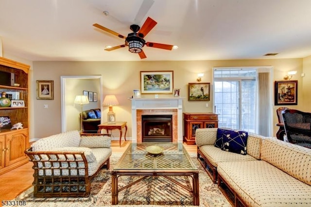 living room featuring ceiling fan, light wood-type flooring, and a fireplace