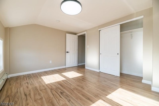 unfurnished bedroom with baseboard heating, a closet, lofted ceiling, and light wood-type flooring