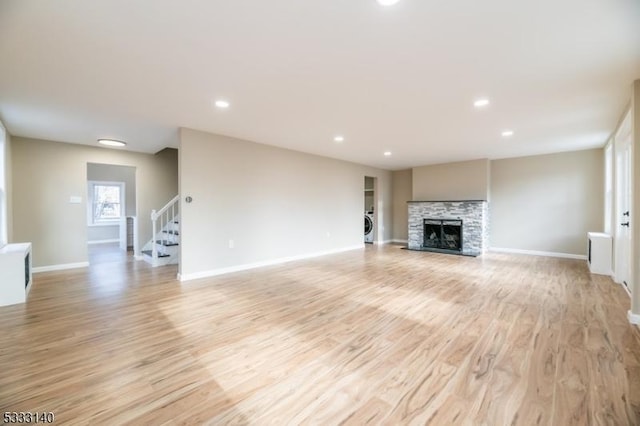 unfurnished living room with washer / clothes dryer, a stone fireplace, and light hardwood / wood-style flooring