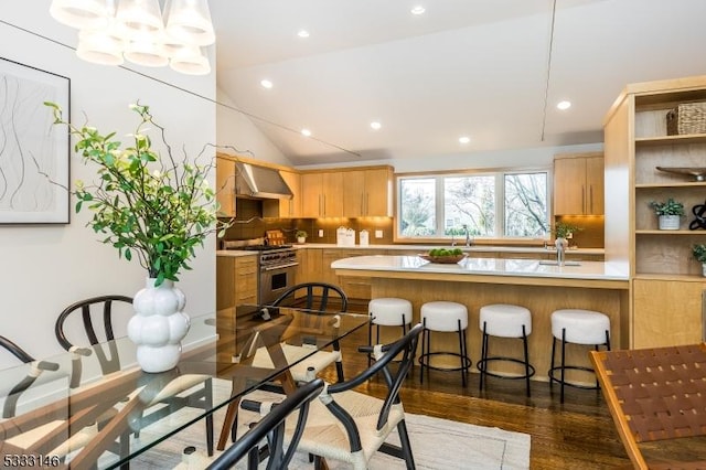 kitchen with lofted ceiling, dark hardwood / wood-style flooring, high end stainless steel range oven, hanging light fixtures, and wall chimney exhaust hood