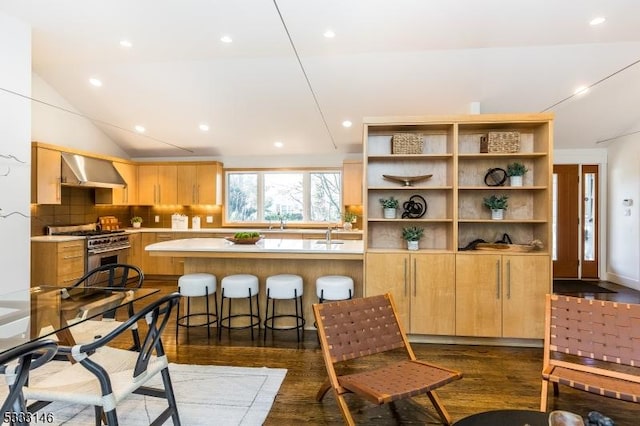 kitchen with kitchen peninsula, backsplash, wall chimney exhaust hood, high end stainless steel range, and a breakfast bar