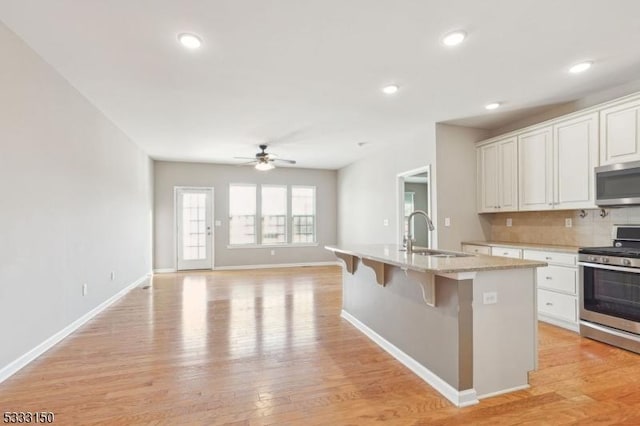 kitchen featuring ceiling fan, a center island with sink, sink, stainless steel appliances, and white cabinets