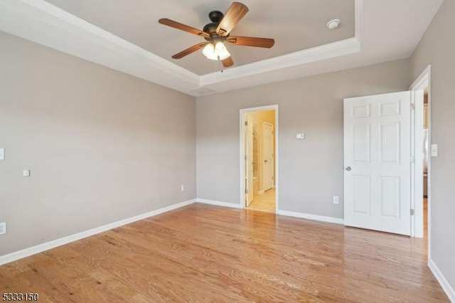 empty room with ceiling fan, a tray ceiling, and light hardwood / wood-style floors