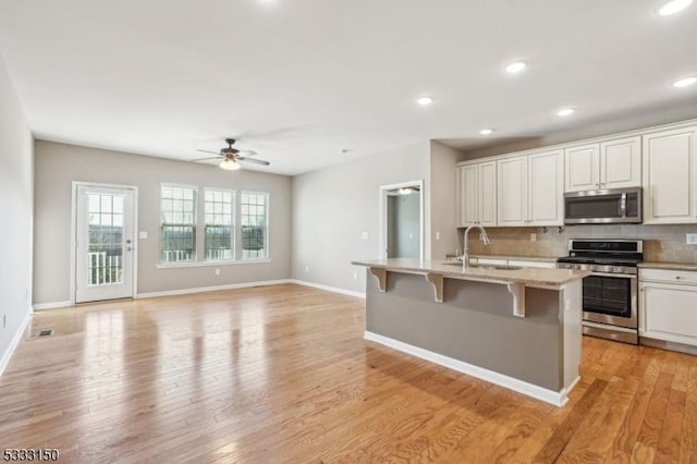 kitchen with white cabinetry, a center island with sink, ceiling fan, appliances with stainless steel finishes, and sink