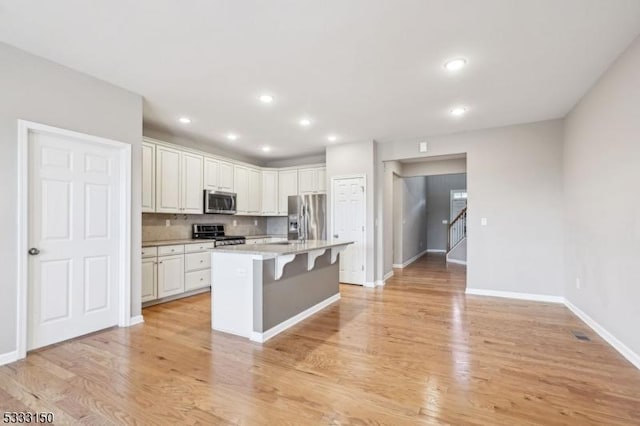 kitchen featuring white cabinetry, stainless steel appliances, an island with sink, backsplash, and a breakfast bar area