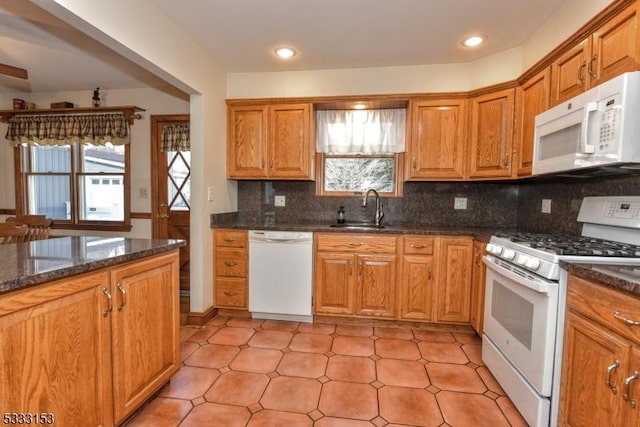 kitchen with decorative backsplash, white appliances, dark stone counters, a wealth of natural light, and sink