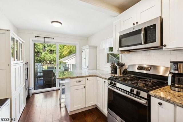 kitchen with decorative light fixtures, kitchen peninsula, light stone countertops, stainless steel appliances, and white cabinets