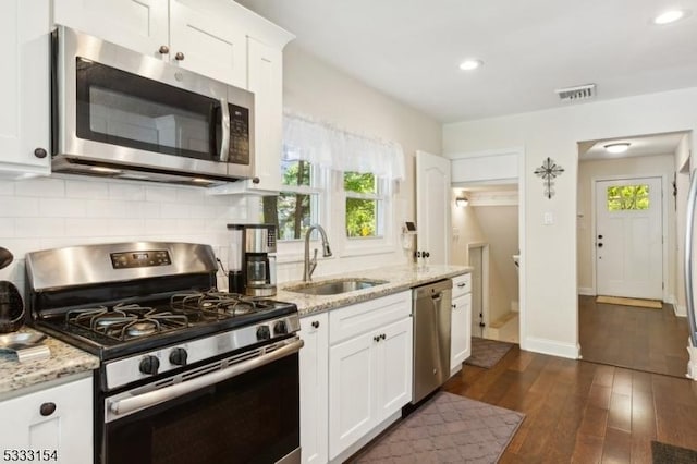 kitchen featuring appliances with stainless steel finishes, dark wood-type flooring, light stone countertops, white cabinets, and sink