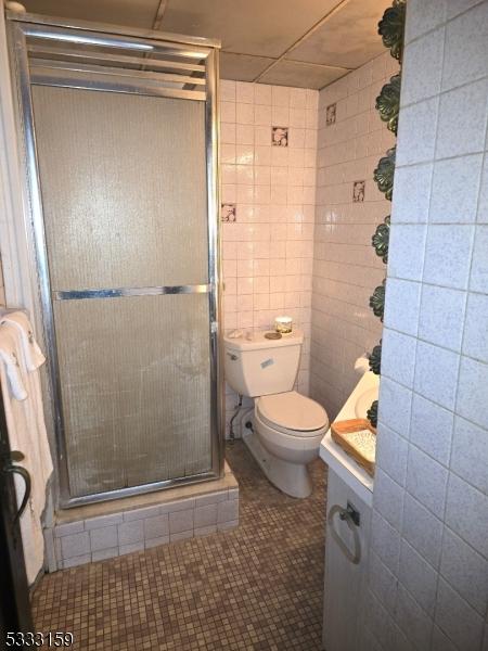 bathroom with tile patterned floors, toilet, a shower with shower door, tile walls, and vanity