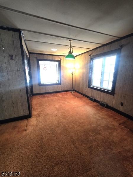 spare room featuring beamed ceiling, carpet floors, and wood walls