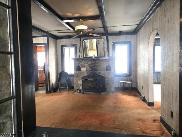 unfurnished living room with ceiling fan, coffered ceiling, carpet floors, beamed ceiling, and a wood stove