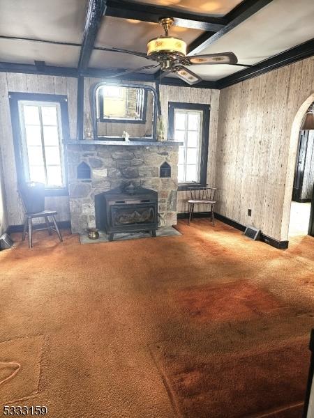 unfurnished living room featuring ceiling fan, carpet flooring, coffered ceiling, beamed ceiling, and a wood stove