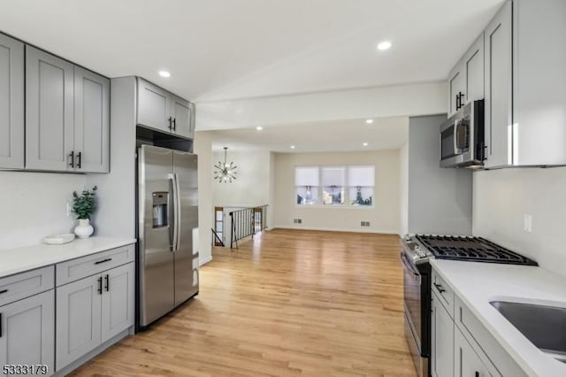 kitchen featuring gray cabinets, sink, light wood-type flooring, appliances with stainless steel finishes, and a chandelier