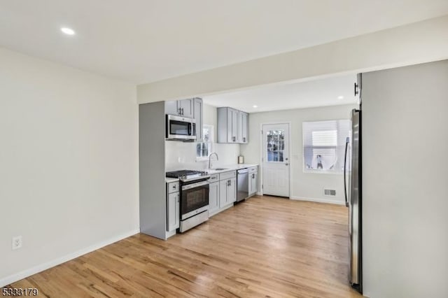 kitchen with appliances with stainless steel finishes, sink, gray cabinetry, and light hardwood / wood-style flooring