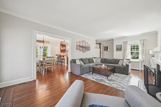 living area with crown molding, a wealth of natural light, wood finished floors, and a chandelier