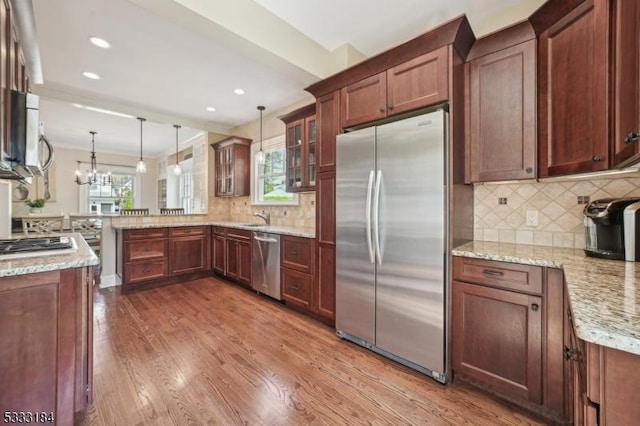 kitchen featuring decorative light fixtures, wood finished floors, a peninsula, glass insert cabinets, and stainless steel appliances