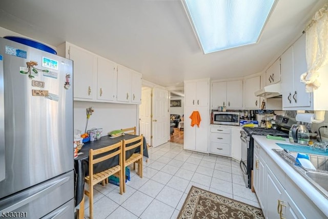 kitchen featuring sink, light tile patterned flooring, white cabinetry, a skylight, and stainless steel appliances