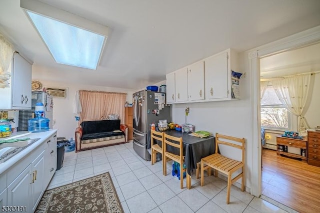 kitchen with light tile patterned flooring, sink, white cabinets, and stainless steel fridge