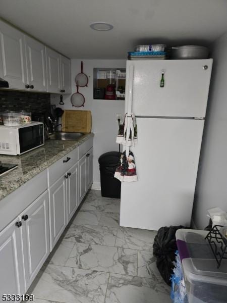 kitchen with backsplash, sink, white appliances, white cabinetry, and light stone counters