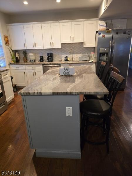 kitchen with white cabinets, light stone counters, stainless steel appliances, and a kitchen island