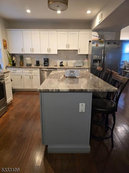 kitchen with dark hardwood / wood-style floors, a kitchen island, stainless steel appliances, white cabinets, and light stone counters