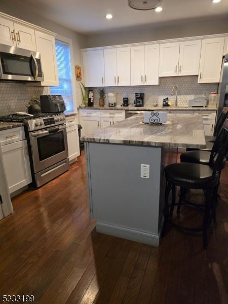 kitchen featuring a center island, white cabinetry, light stone countertops, stainless steel appliances, and dark hardwood / wood-style flooring