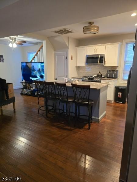 kitchen featuring ceiling fan, dark hardwood / wood-style floors, appliances with stainless steel finishes, a kitchen breakfast bar, and white cabinets