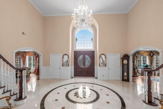 foyer entrance with ornamental molding, a towering ceiling, and an inviting chandelier