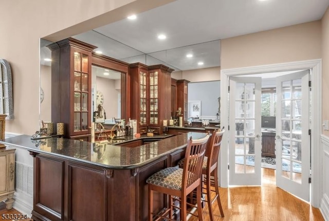 bar with light wood-type flooring, french doors, and dark stone counters