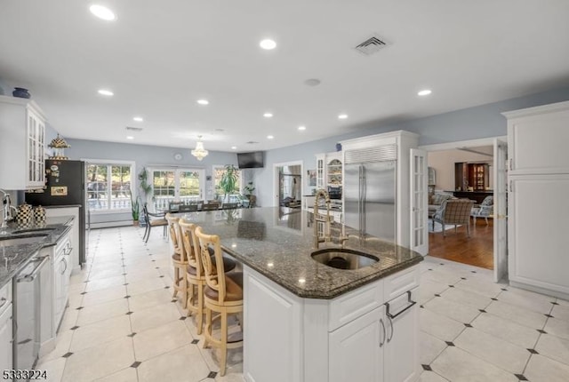 kitchen with stainless steel appliances, a spacious island, dark stone counters, white cabinets, and sink