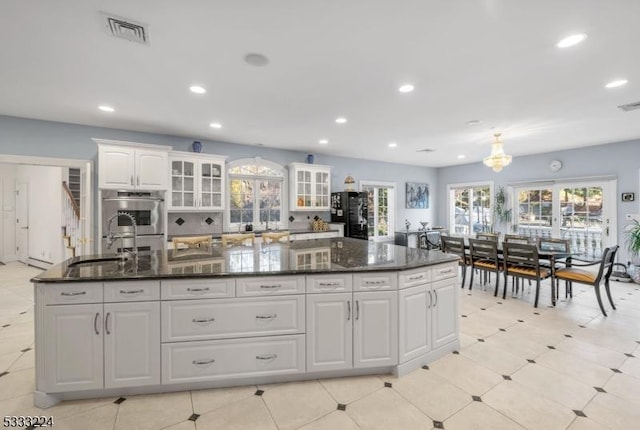 kitchen featuring white cabinetry, black refrigerator, an island with sink, dark stone countertops, and sink