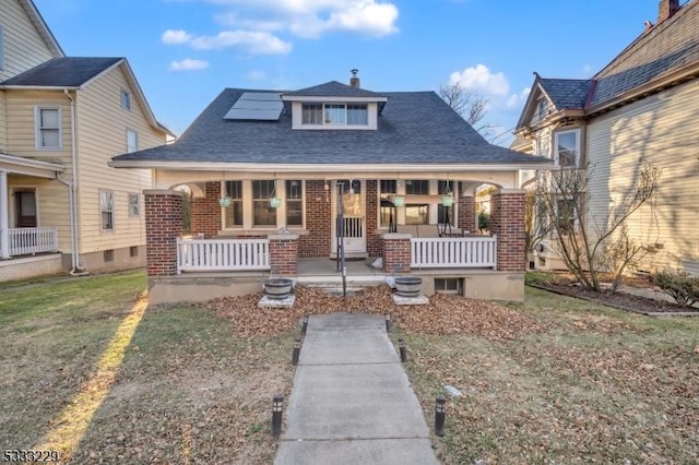 view of front of home featuring a front yard, a porch, and solar panels