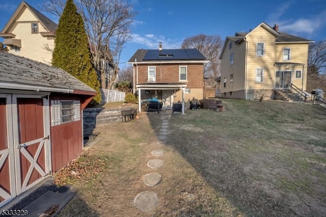 back of house with a yard, a storage shed, and solar panels