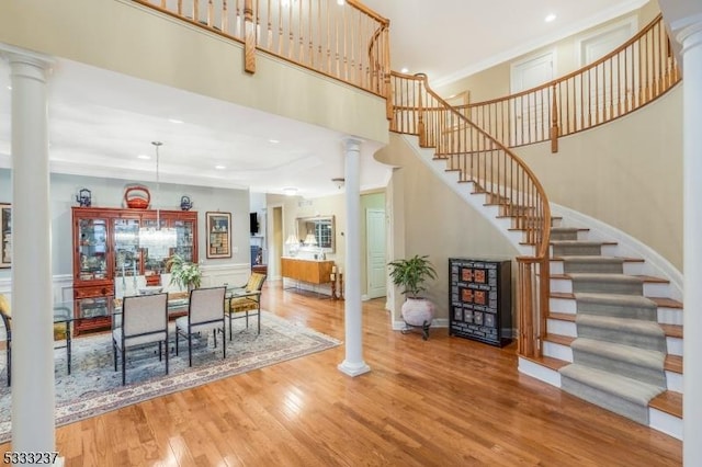 dining space with a towering ceiling, wood finished floors, stairs, ornate columns, and recessed lighting